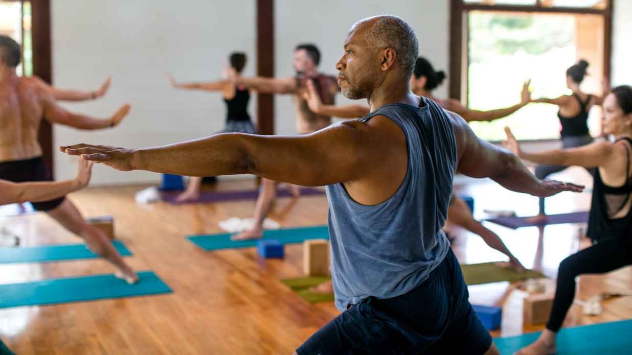 Man doing warrior 2 yoga pose in a class with other students