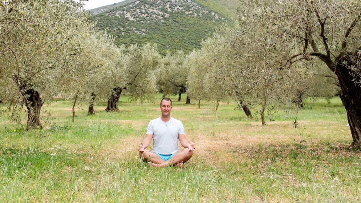 Yogi Aaron in crossed legged seated position meditating in nature setting