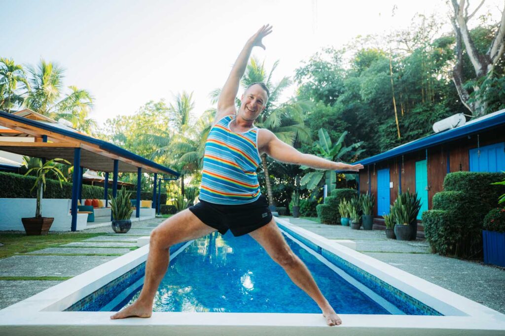 Yogi Aaron Doing Warrior Yoga Pose on Blue Osa Pool Ledge