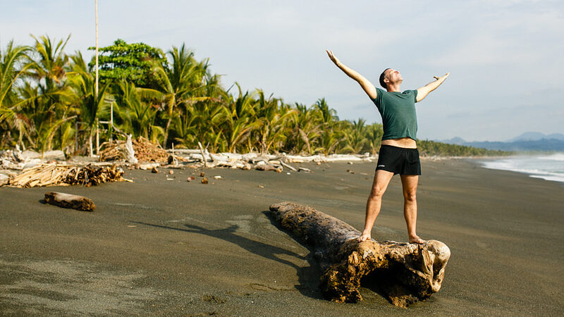 Yogi Aaron on the beach at Blue Osa with arms stretched up and out in a grateful gesture for all of life.