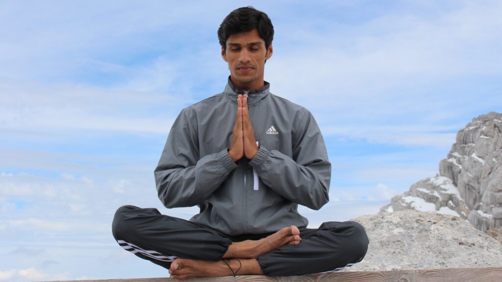 Indian Man sitting on mountain in cross-legged position doing Namaste mudra