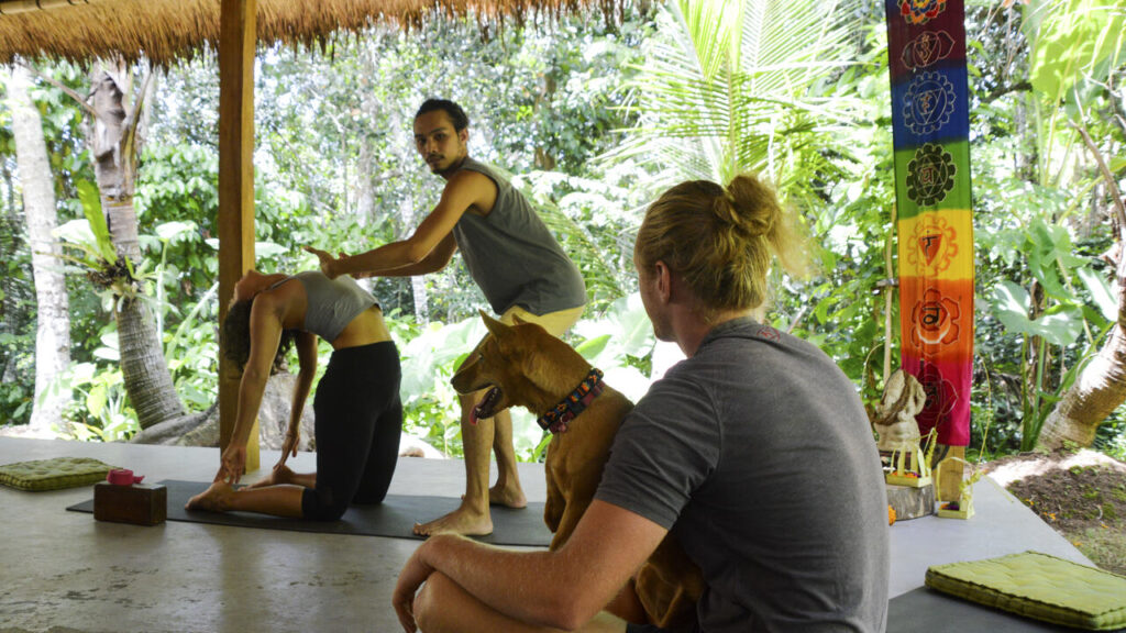 male yoga teacher adjusting student in camel pose yoga students watching